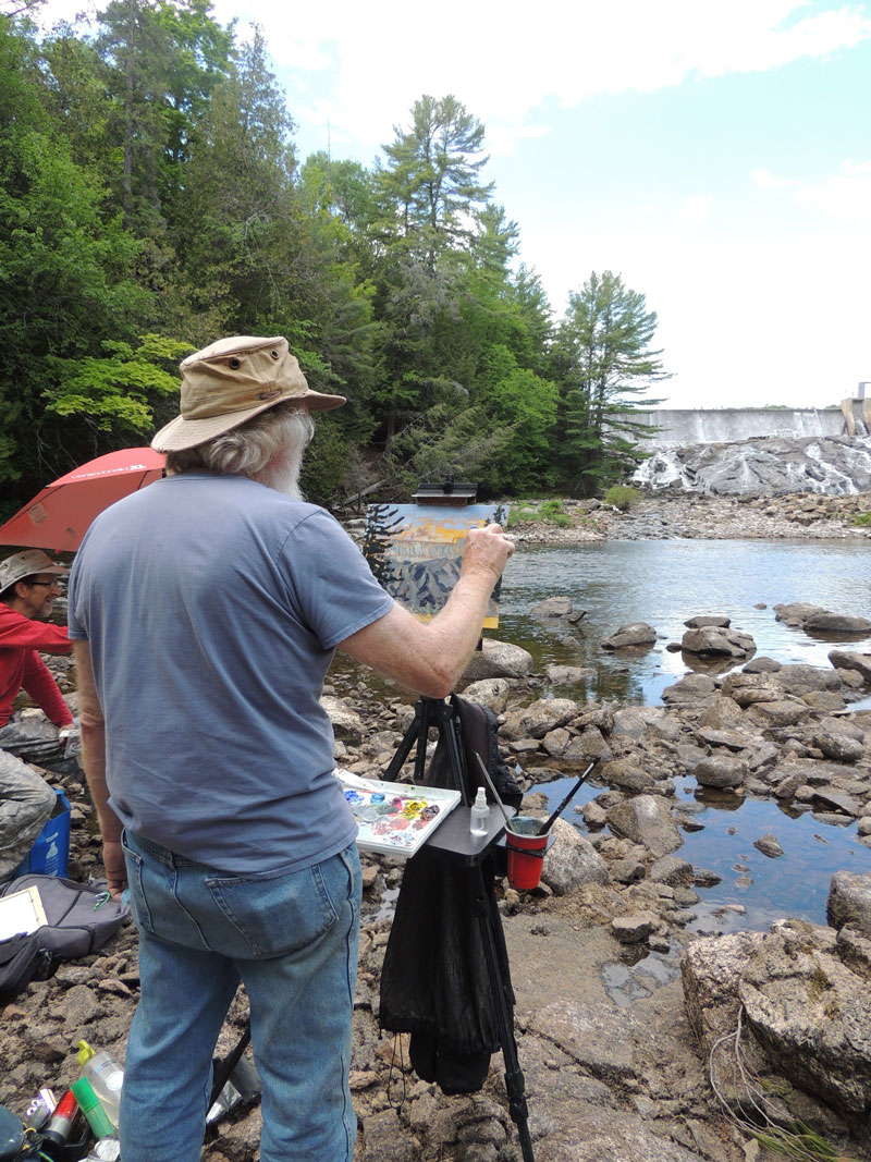 Artist painting nature scene on a canvas outside by waterfall. Plein Air Workshop in Bancroft Ontario