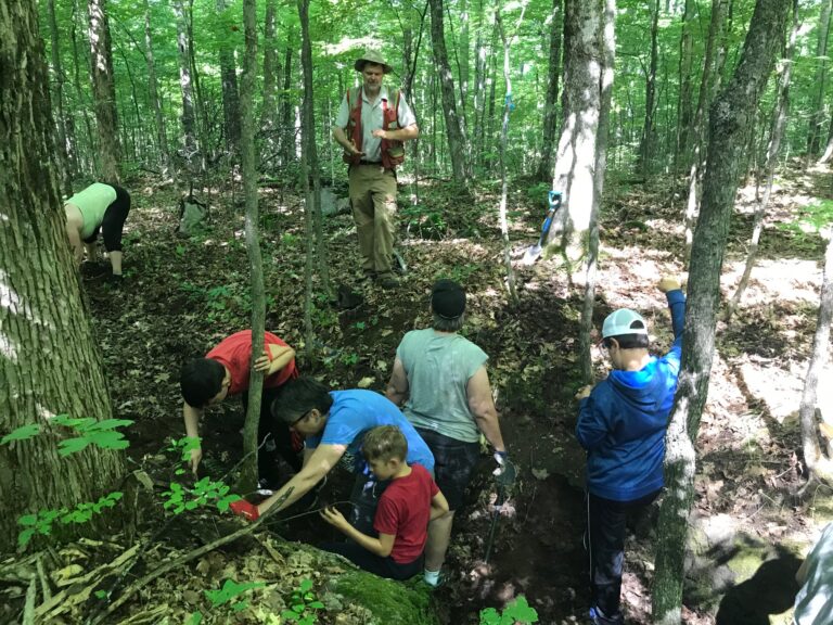 A group of people in the woods working on collecting mineral specimens from the ground