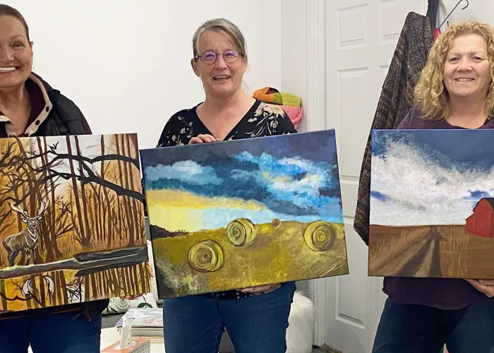 Three people holding paintings that they have made