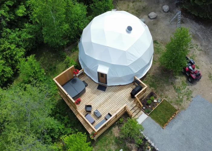 A white glamping dome site next to a wooden dock. With a red ATV beside it and green trees in the background.