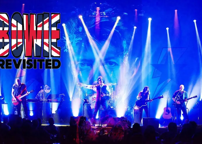 Six band members on stage, dramatic stage lighting, David Bowie's face in background