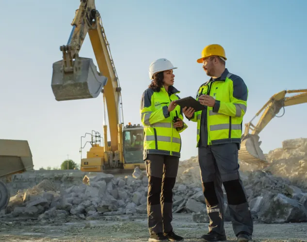 Two people on a construction site with construction equipment in background.
