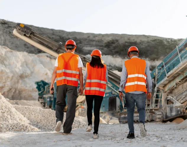 People walking at a quarrying site. Three people in total with orange high visibility vests on. 
